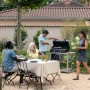 Grigliata in giardino: persone sedute a tavola, un uomo griglia. Atmosfera da campeggio con t.b.t.