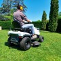 Trattorino tagliaerba in azione: uomo che taglia l'erba con protezioni acustiche gialle.