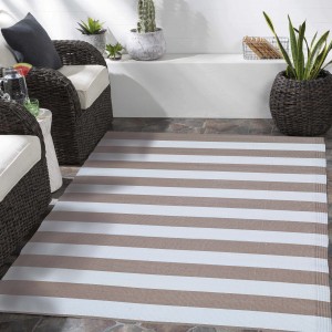 Tappeto da esterno a righe beige e bianco su un patio con mobili da giardino.