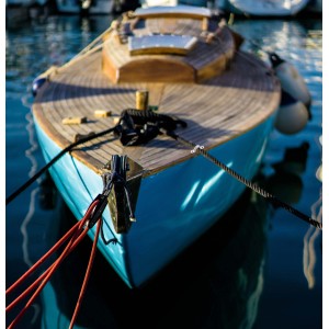 Primo piano di una barca a vela blu con ponte in legno e accessori nautici.