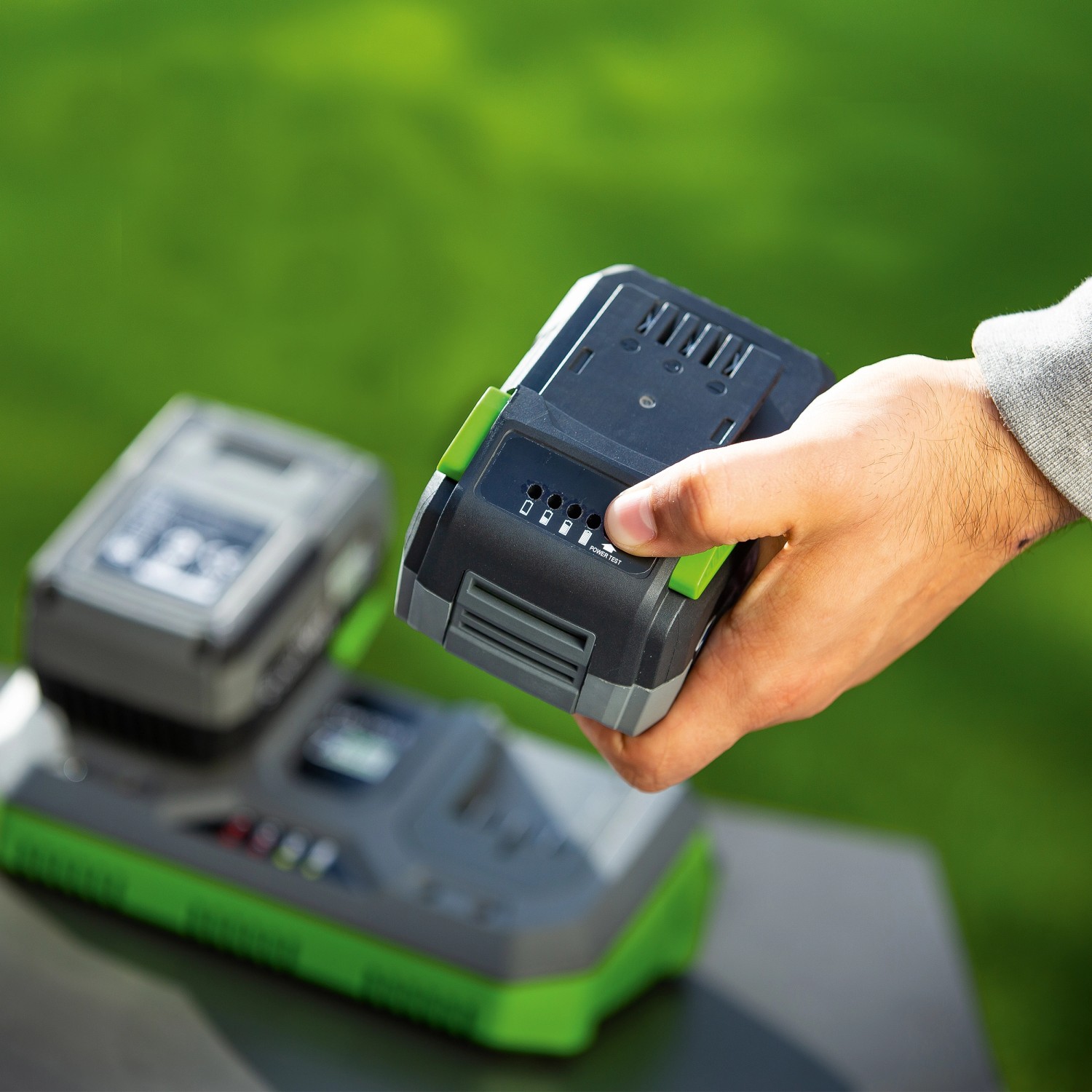 LUX 1 PowerSystem Starter Set: batteria da 20 V (4 Ah) con caricabatterie in mano sopra la stazione di ricarica.
