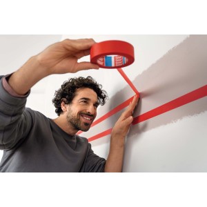 Uomo che applica nastro adesivo rosso t.b.t. a una parete.