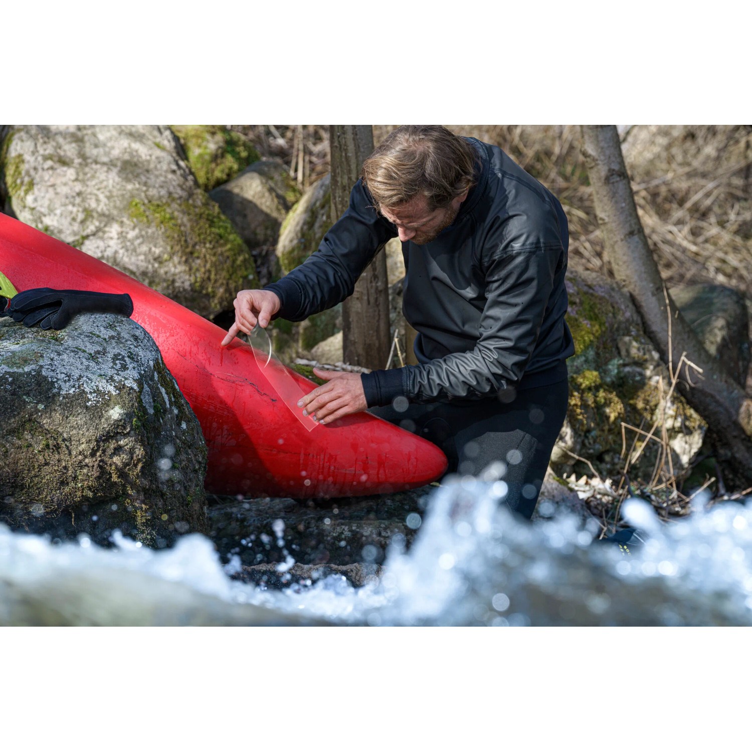 Uomo ripara kayak rosso con nastro riparatore trasparente Tesa Ultra Power Under Water all'aperto.