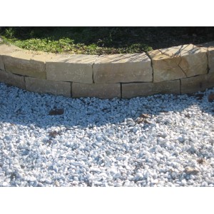 Ciottoli e granulati decorativi chiari davanti a un muro in pietra naturale.