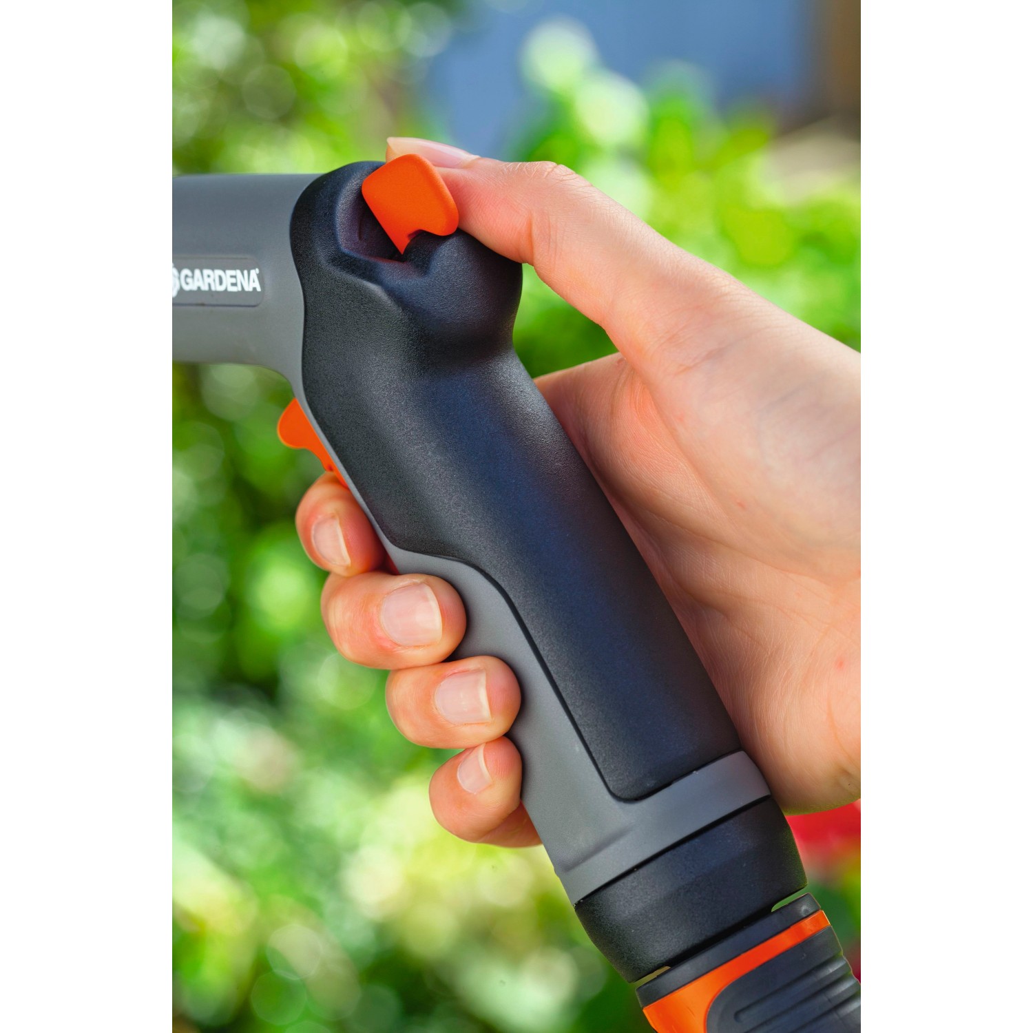 Mano che tiene la pistola a spruzzo Gardena Classic, spruzzatore da giardino con grilletto arancione.