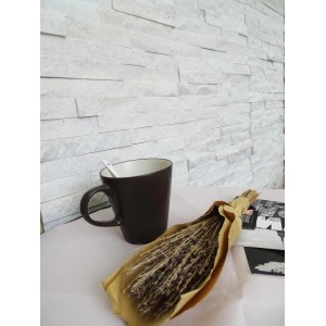 Parete in pietra naturale chiara con tazza e bouquet di lavanda come decorazione.