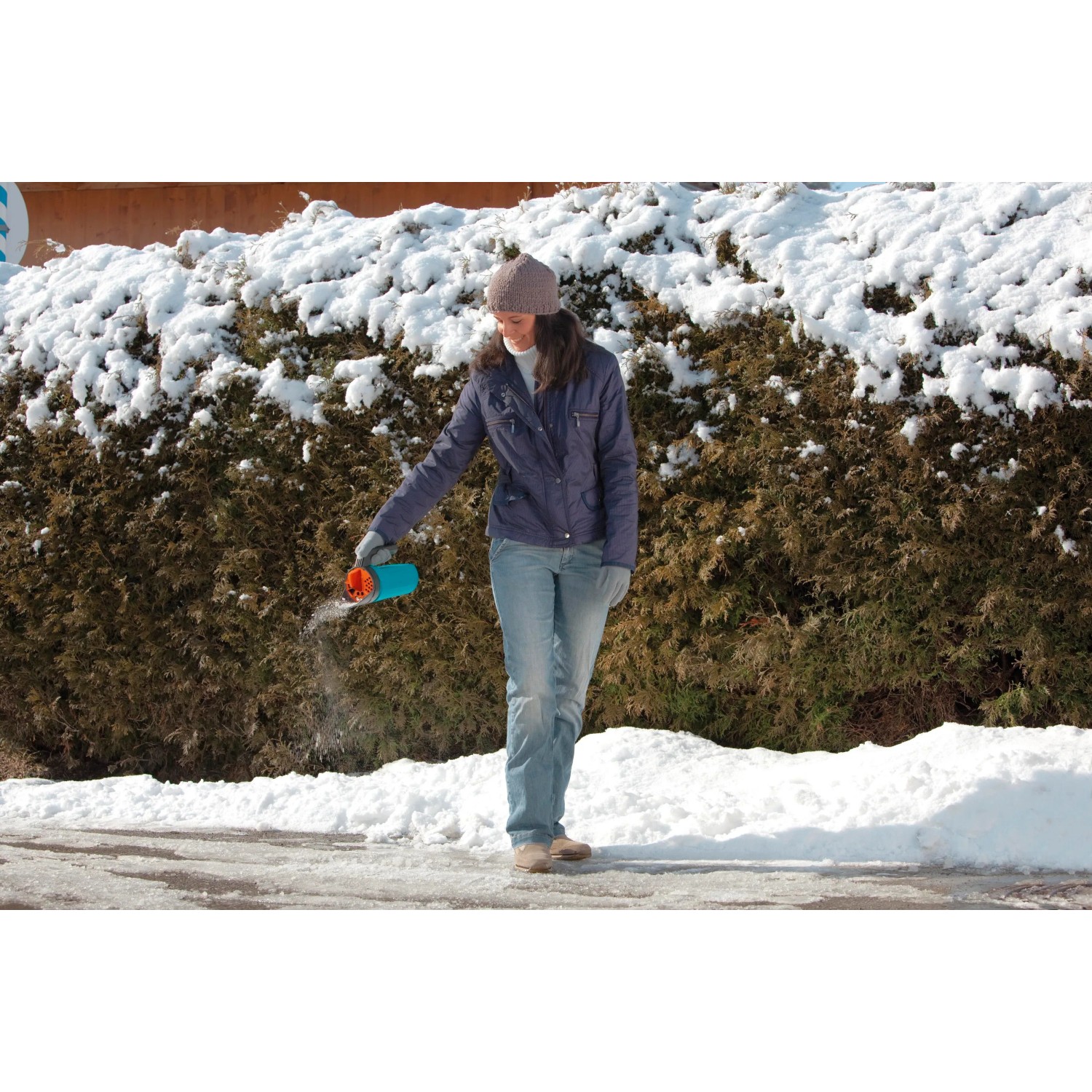 Donna sparge sale antigelo con spargisale Gardena Kleinstreuer S turchese su superficie ghiacciata.