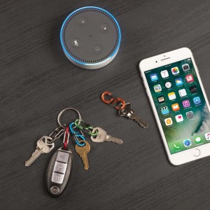 Portachiavi con chiavi, smartphone e smart speaker su tavolo scuro.