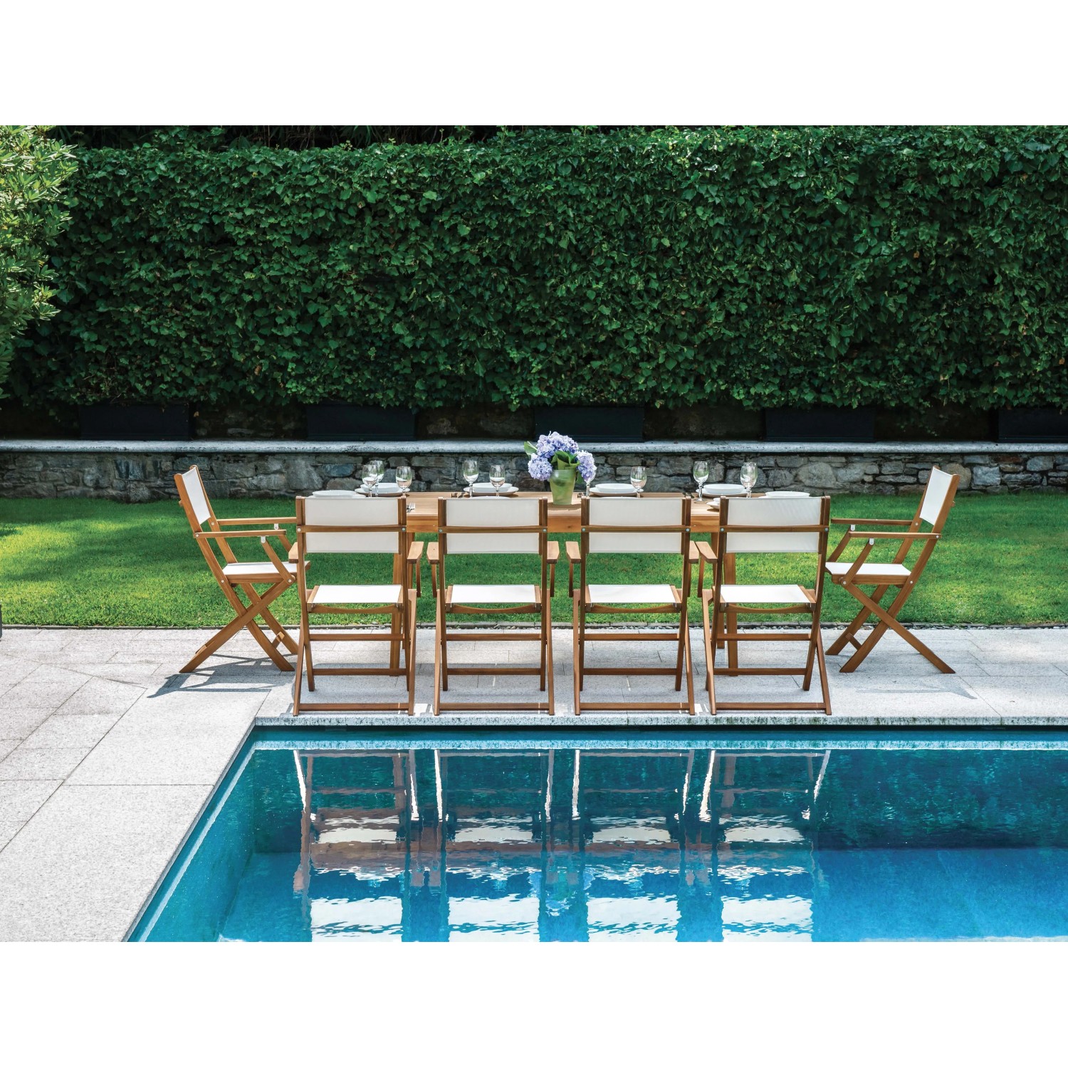 Set tavolo da giardino t.b.t. con struttura in legno e sedie bianche a bordo piscina.