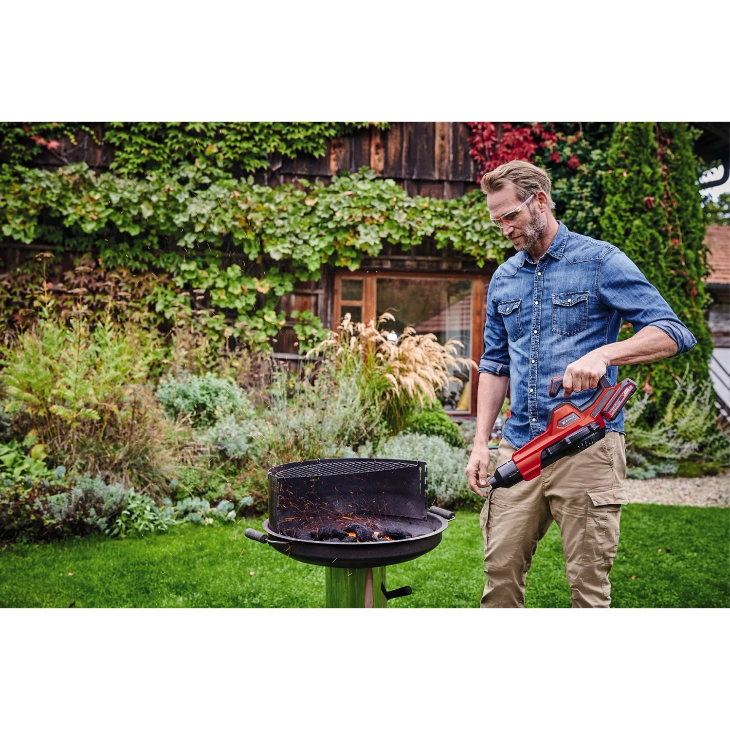 Uomo che accende la griglia con soffiatore a batteria rosso Einhell GE-UB 18/250 Li E-Solo in giardino.