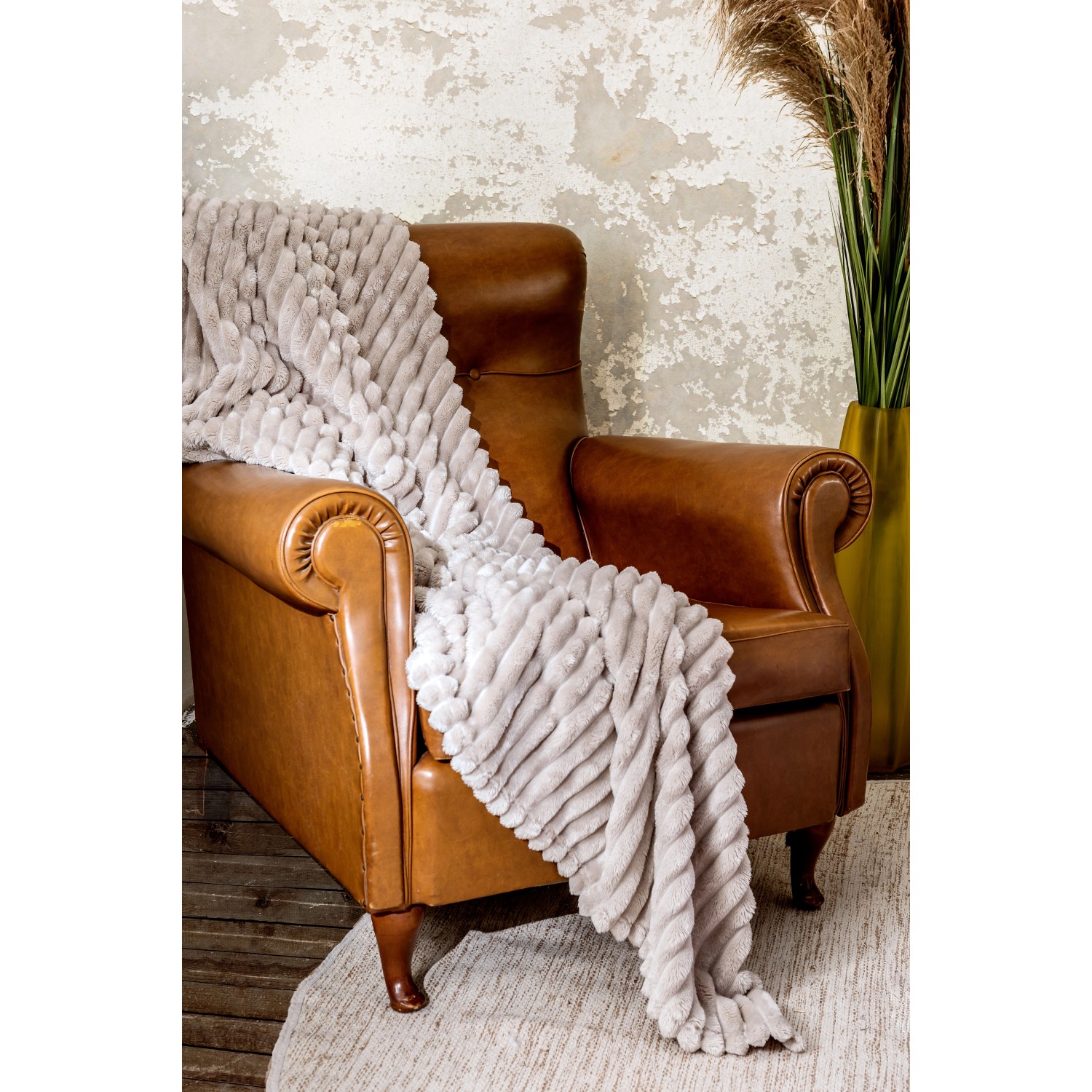 Morbida coperta t.b.t. grigio chiaro drappeggiata su una poltrona in pelle marrone. Plaid accogliente per soggiorno o camera da letto.