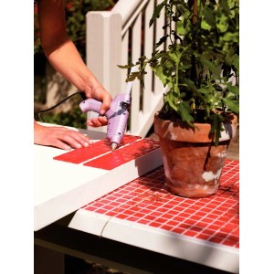 Applicazione di una pistola per colla a caldo su piastrelle a mosaico rosse. Progetto fai-da-te.
