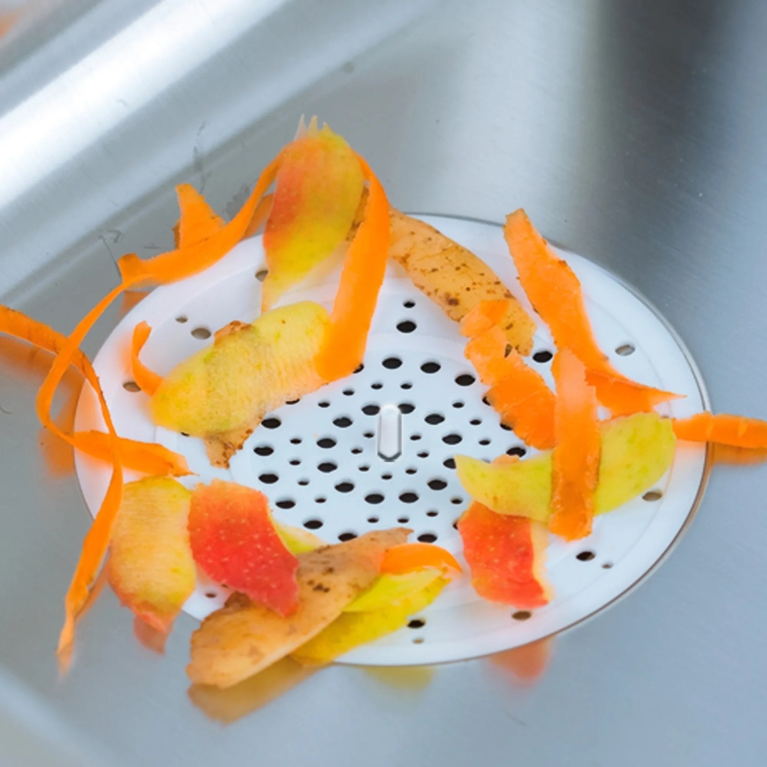 Filtro di scarico Wenko bianco in silicone nel lavello con scarti di verdure.