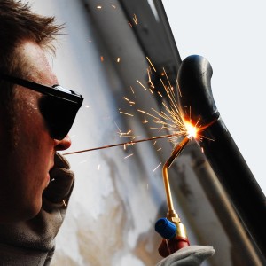 Saldatore al lavoro con attrezzatura e protezioni. Accessori per saldatura.