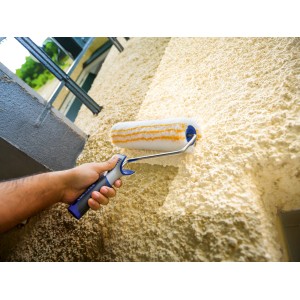 Rullo a dispersione LUX 25 cm in uso su parete ruvida. Rullo per pittura con manico blu-grigio.