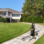 Idropulitrice con accessori su un sentiero lastricato davanti a casa e giardino.