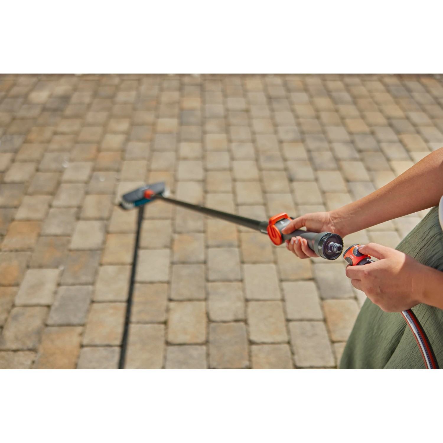 Gardena Cleansystem Spazzola a setole dure con raccordo per tubo flessibile in uso per la pulizia di pavimentazioni.