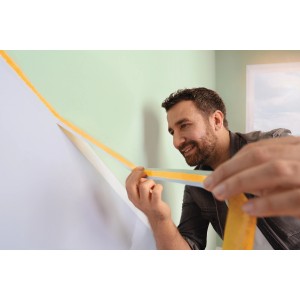 Uomo che applica tesa® Malerband Perfect+ a una parete per bordi di vernice netti.