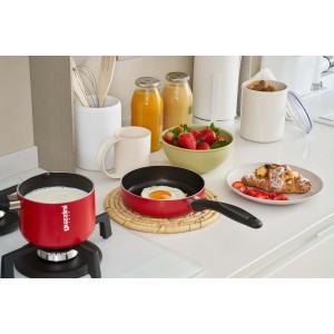 Padella rossa t.b.t. con uovo fritto e pentolino per il latte su un tavolo da cucina.