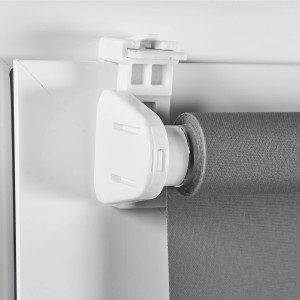 Dettaglio di una tenda a rullo t.b.t. grigia con staffa bianca sul telaio della finestra.