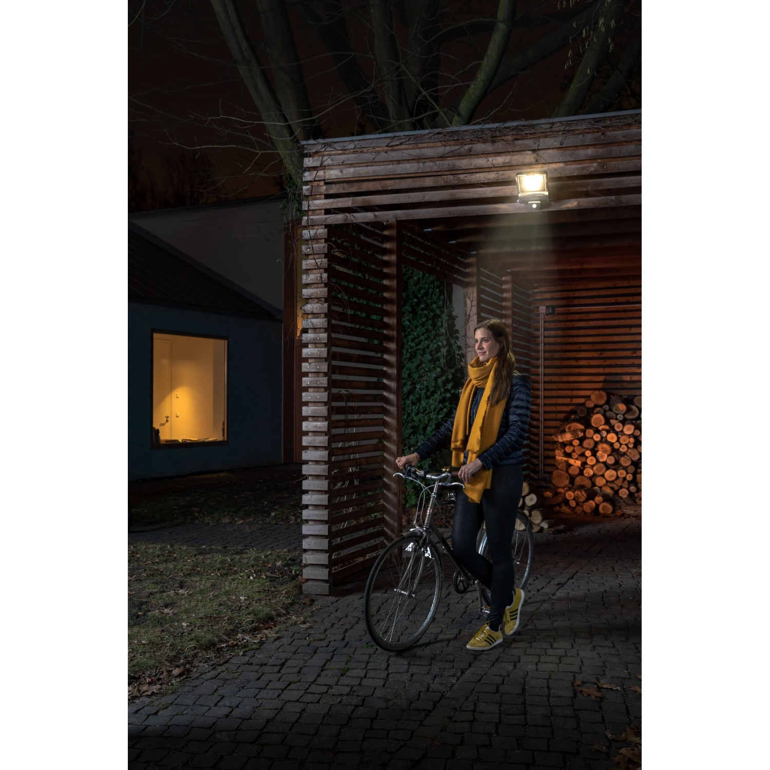 Faretto LED da esterno Ledvance Endura Flood grigio scuro con sensore illumina donna con bicicletta.
