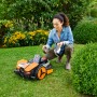 Donna accovacciata accanto al robot tagliaerba Worx Landroid Vision M600 in giardino.