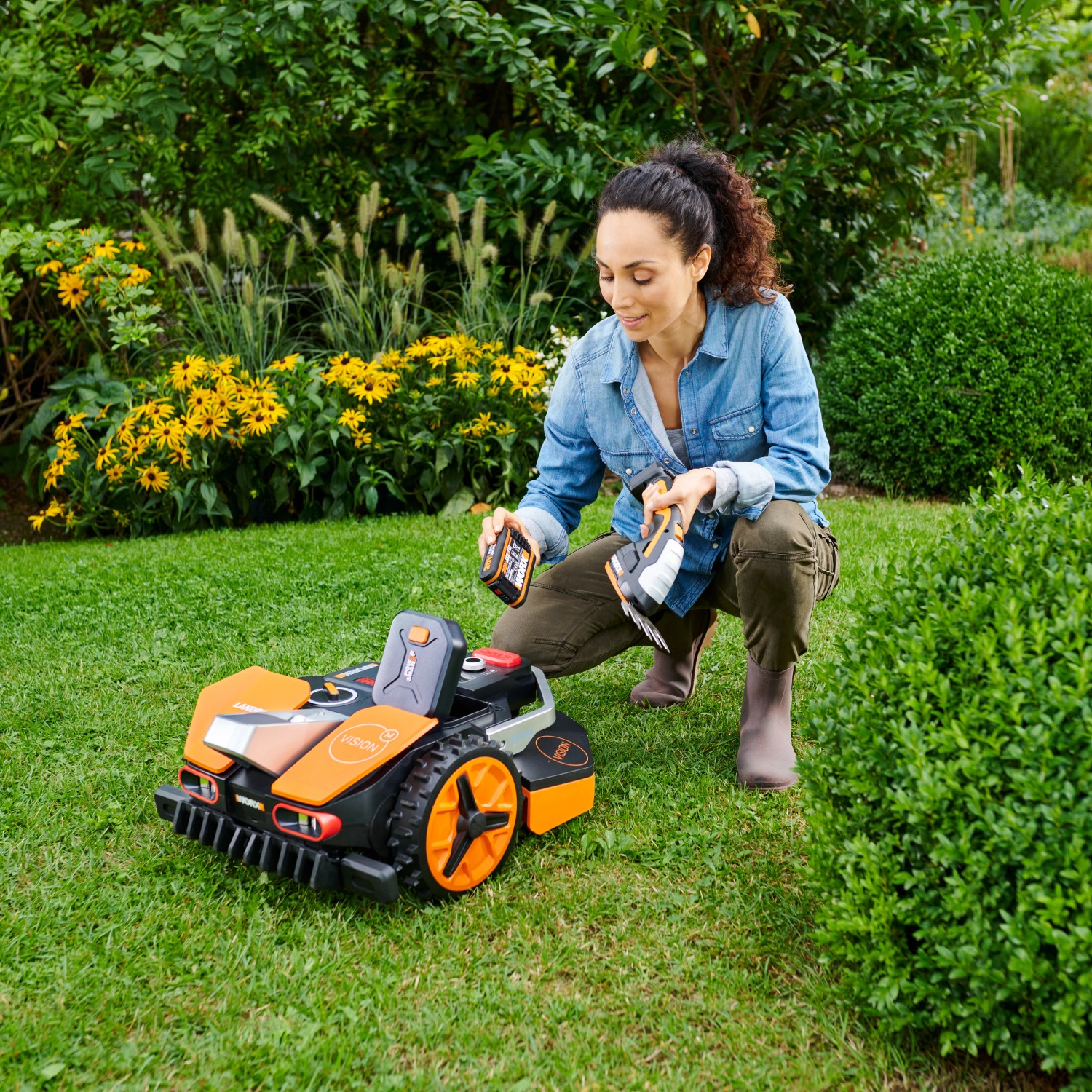 Donna accovacciata accanto al robot tagliaerba Worx Landroid Vision M600 in giardino.