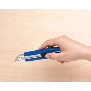 Mano che tiene un cutter LUX Classic 100 mm blu su sfondo di legno chiaro.