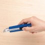 Mano che tiene un cutter LUX Classic 100 mm blu su sfondo di legno chiaro.