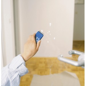 Mano che utilizza il raschietto universale LUX con lama per rimuovere schizzi di vernice sul vetro.