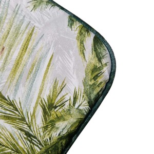 Dettaglio di un cuscino da esterno con motivo a foglie tropicali e bordo verde.