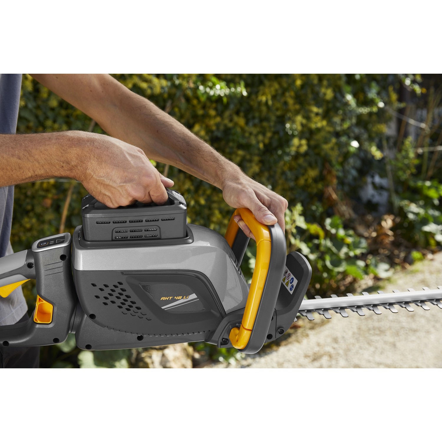 Tagliasiepi a batteria t.b.t. in azione, corpo grigio, manico giallo e batteria inserita.
