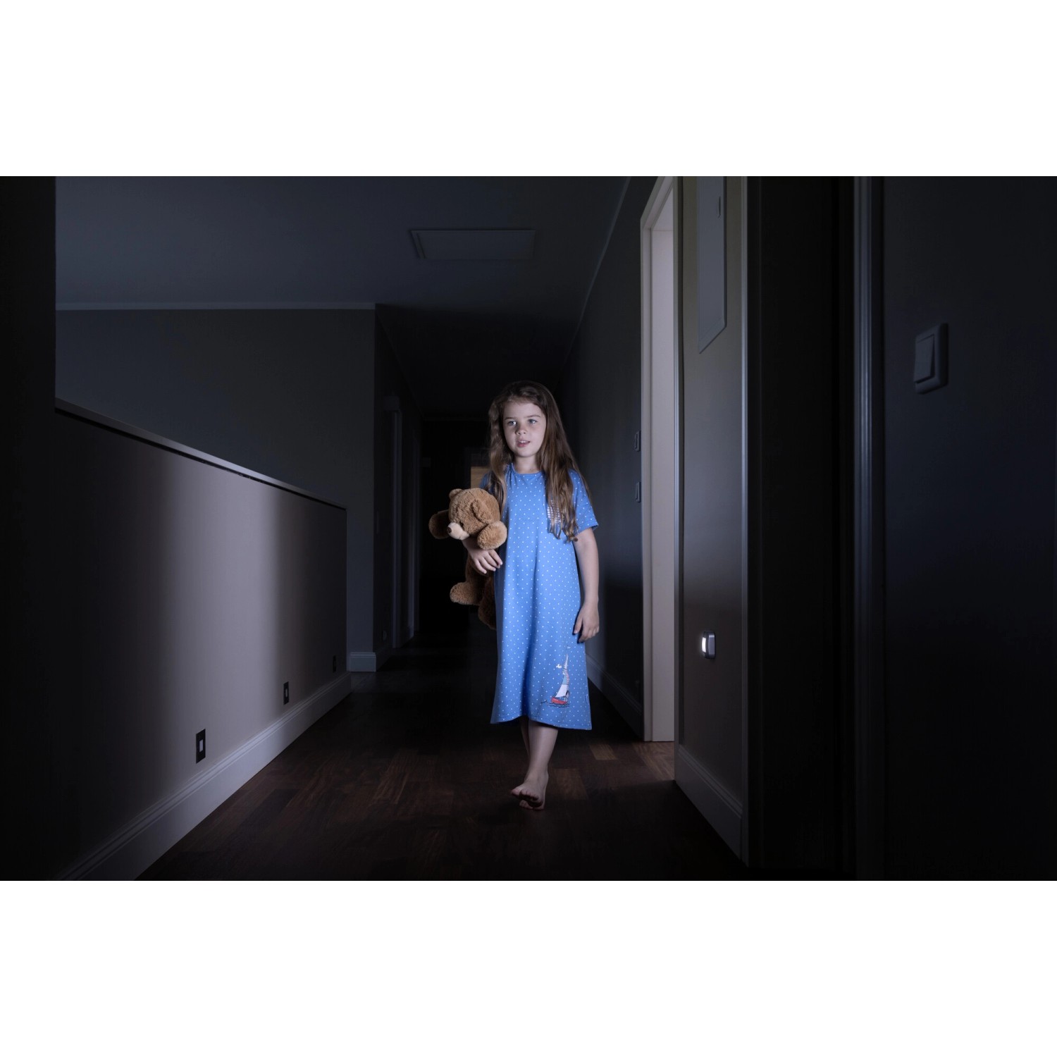 Bambina con orsacchiotto in corridoio, illuminata dalla luce notturna a LED Ledvance Nightlux in argento.
