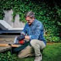 Uomo che sega legno con la sega circolare a mano rossa Einhell TC-CS 1250 in giardino.