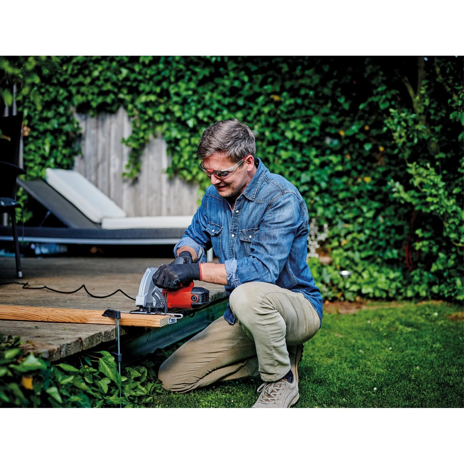 Uomo che sega legno con la sega circolare a mano rossa Einhell TC-CS 1250 in giardino.
