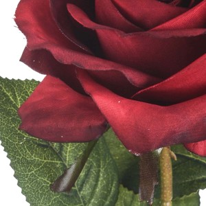 Primo piano di una rosa artificiale rosso scuro con foglie verdi.