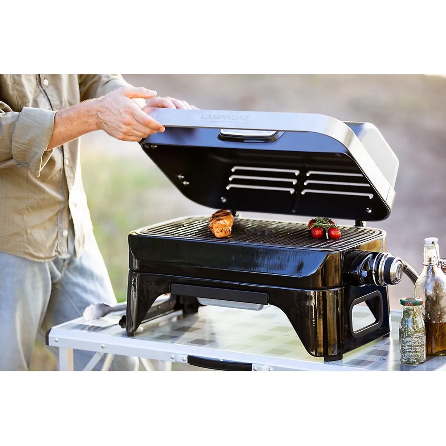 Campingaz Barbecue a gas Attitude 2go CV con cibo sulla griglia, barbecue da tavolo per campeggio e balcone.