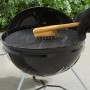 Spazzola per griglia Weber con manico in bambù pulisce la griglia. Barbecue a carbone sullo sfondo.