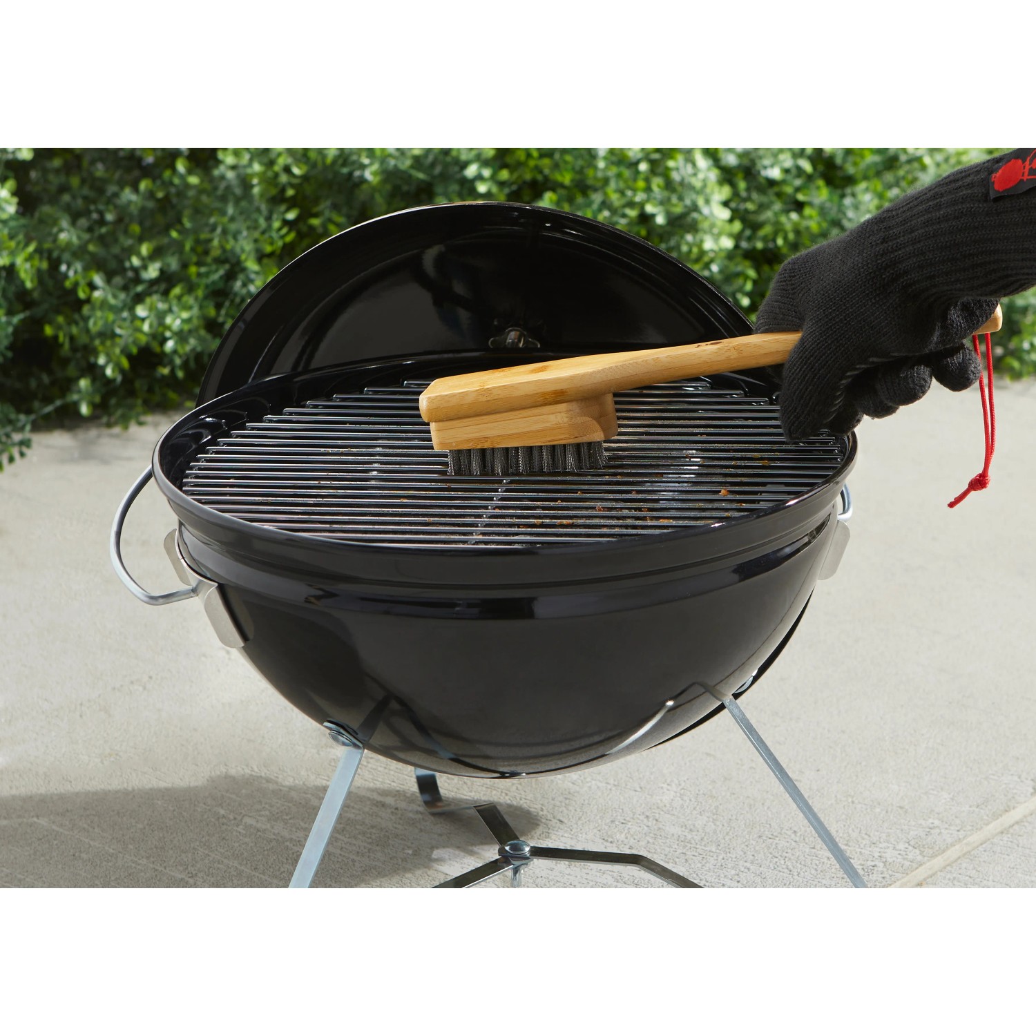 Spazzola per griglia Weber con manico in bambù pulisce la griglia. Barbecue a carbone sullo sfondo.