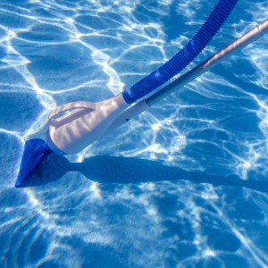 Aspiratore manuale per piscina Gre in piscina, vasca blu, tubo di aspirazione e asta telescopica visibili.