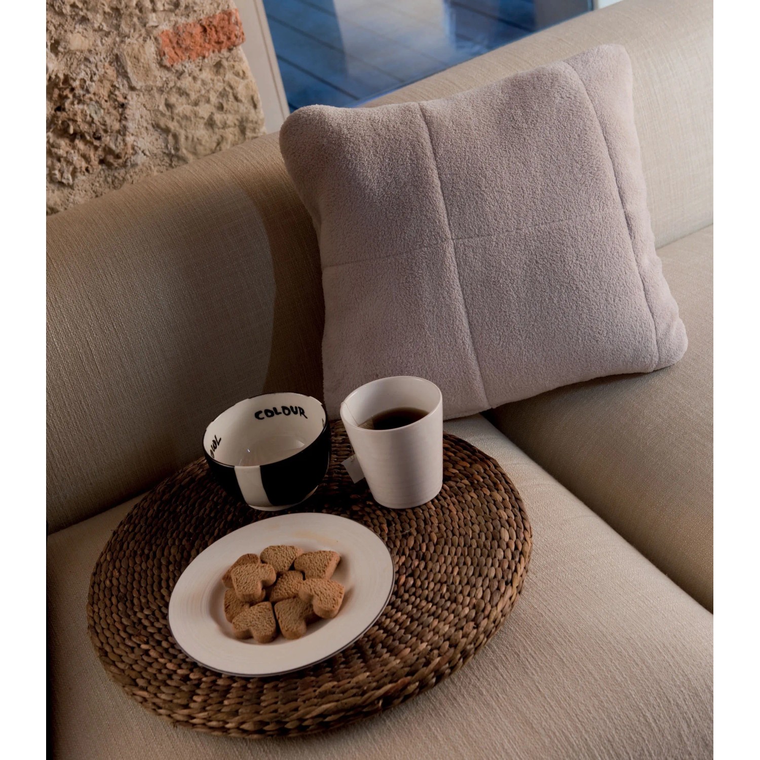 Coperta/plaid t.b.t. beige usata come cuscino su divano con bevande e biscotti.