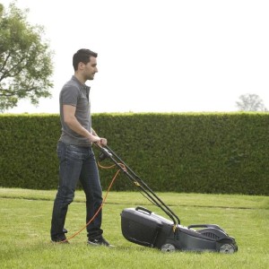 Uomo che taglia l'erba con tosaerba elettrico t.b.t. in giardino.
