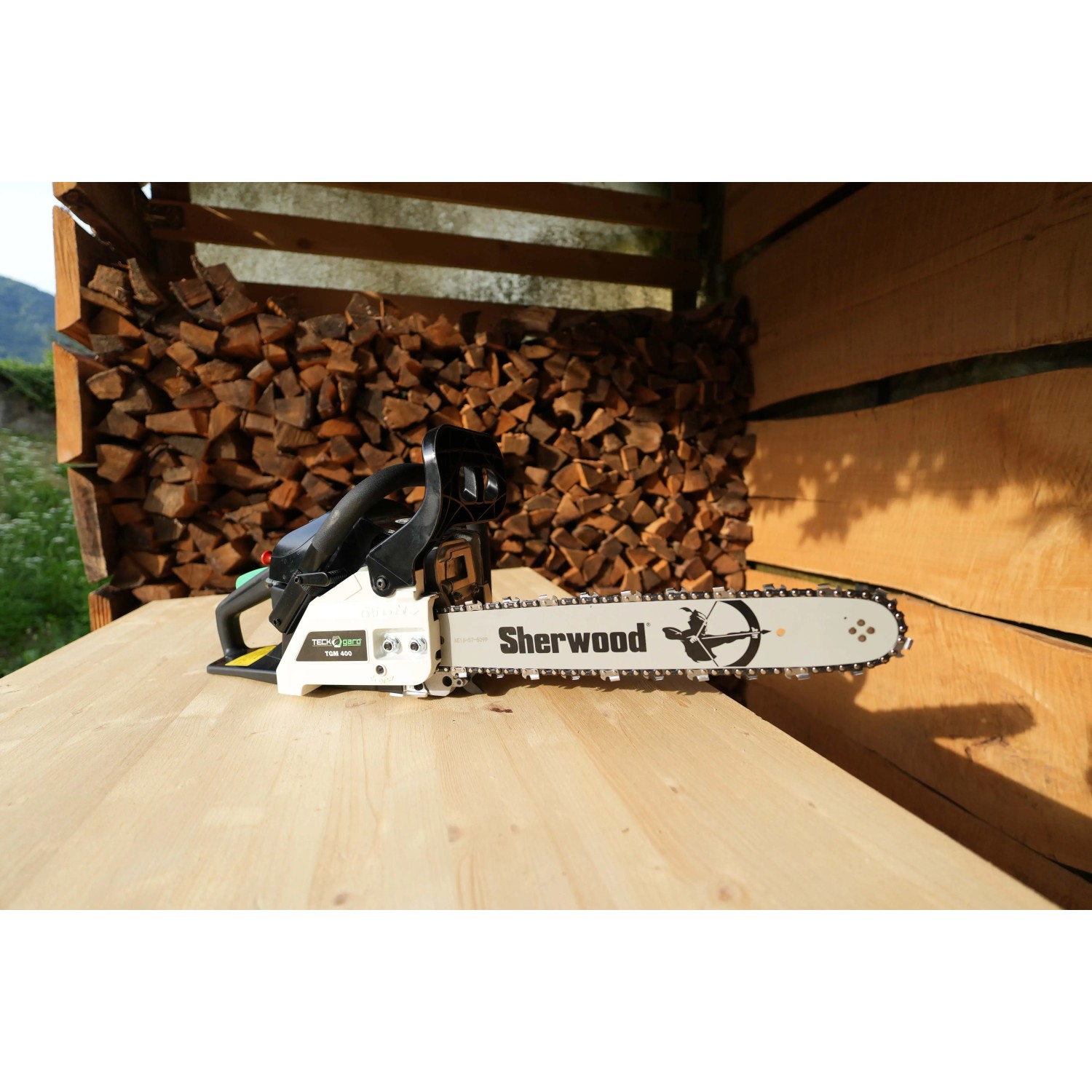 Motosega t.b.t. su tavolo di legno davanti a catasta di legna.