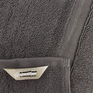 Dettaglio di un tappeto da bagno t.b.t. grigio con etichetta.