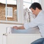 Uomo installa Tesamoll Heat Reflector dietro il radiatore per la riflessione del calore.