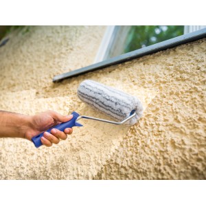 Mano che dipinge parete ruvida con rullo a dispersione LUX 25 cm. Rullo per pittura con manico blu.