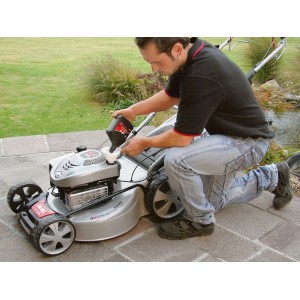 Uomo che versa olio in un tosaerba argentato. Accessori per tosaerba.