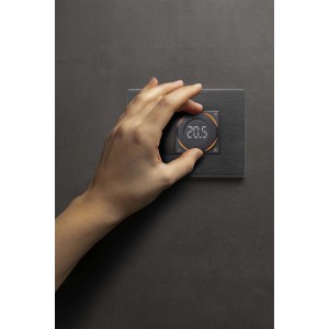 Mano che aziona il termostato t.b.t. con display digitale su parete grigia.