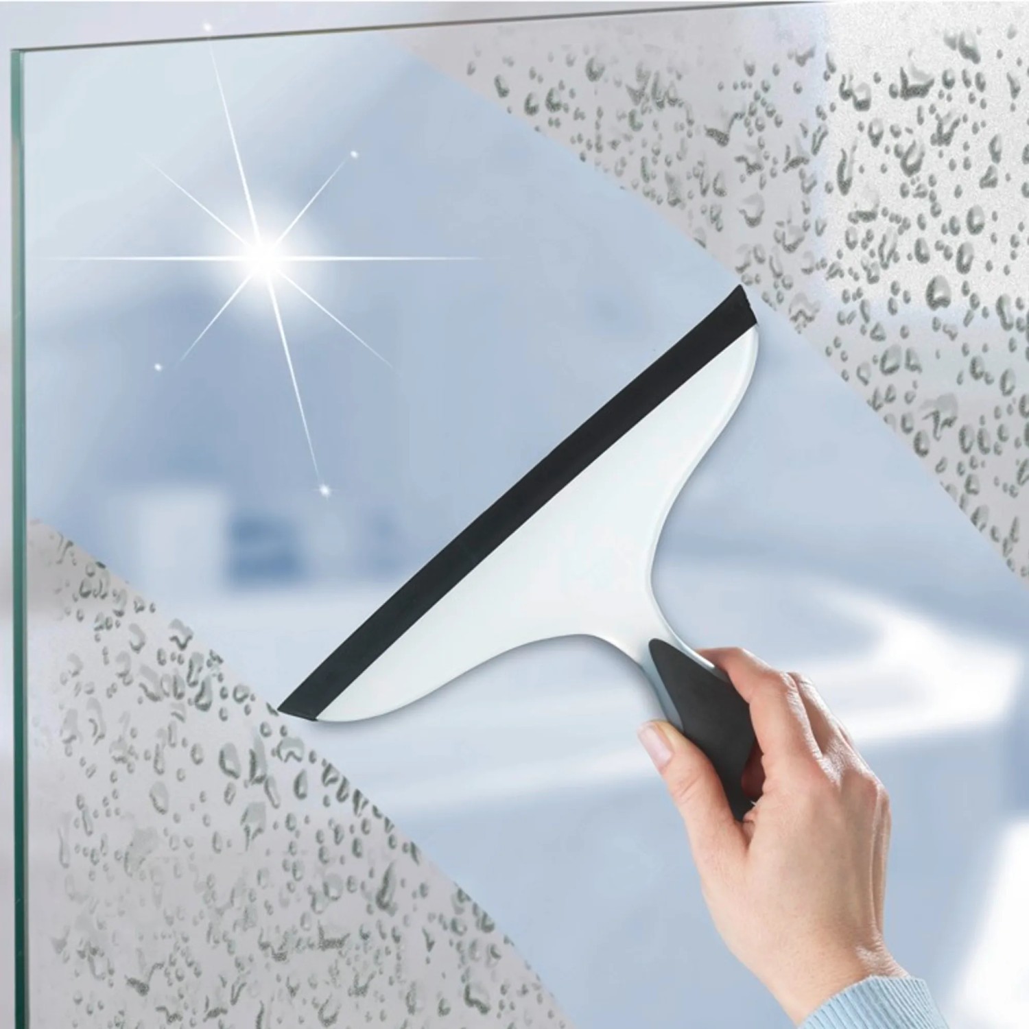 Il tergivetro doccia Wenko Loano in bianco e nero pulisce una parete doccia dalle gocce d'acqua.