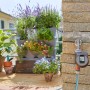 Irrigatore Gardena Flex collegato al rubinetto con balcone piantumato sullo sfondo.